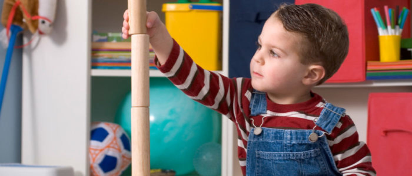 Young boy building tower with cylindrical wooden blocks