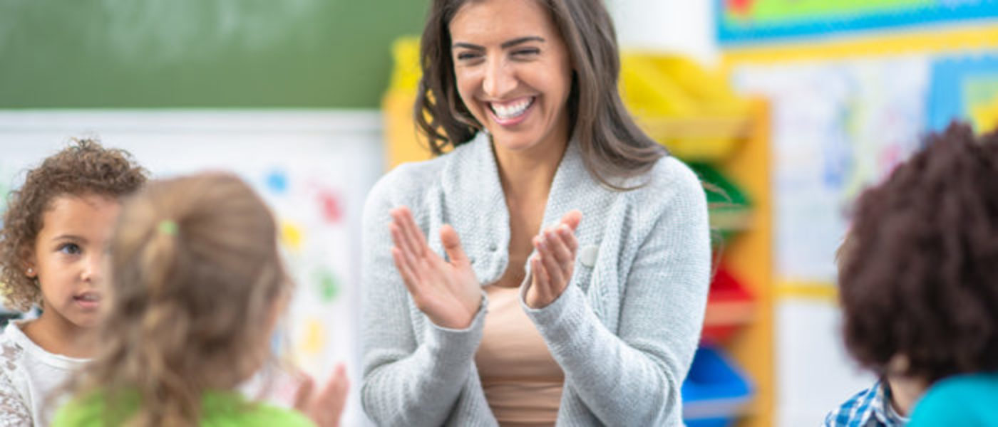 Female teacher smiles and claps with group of young children
