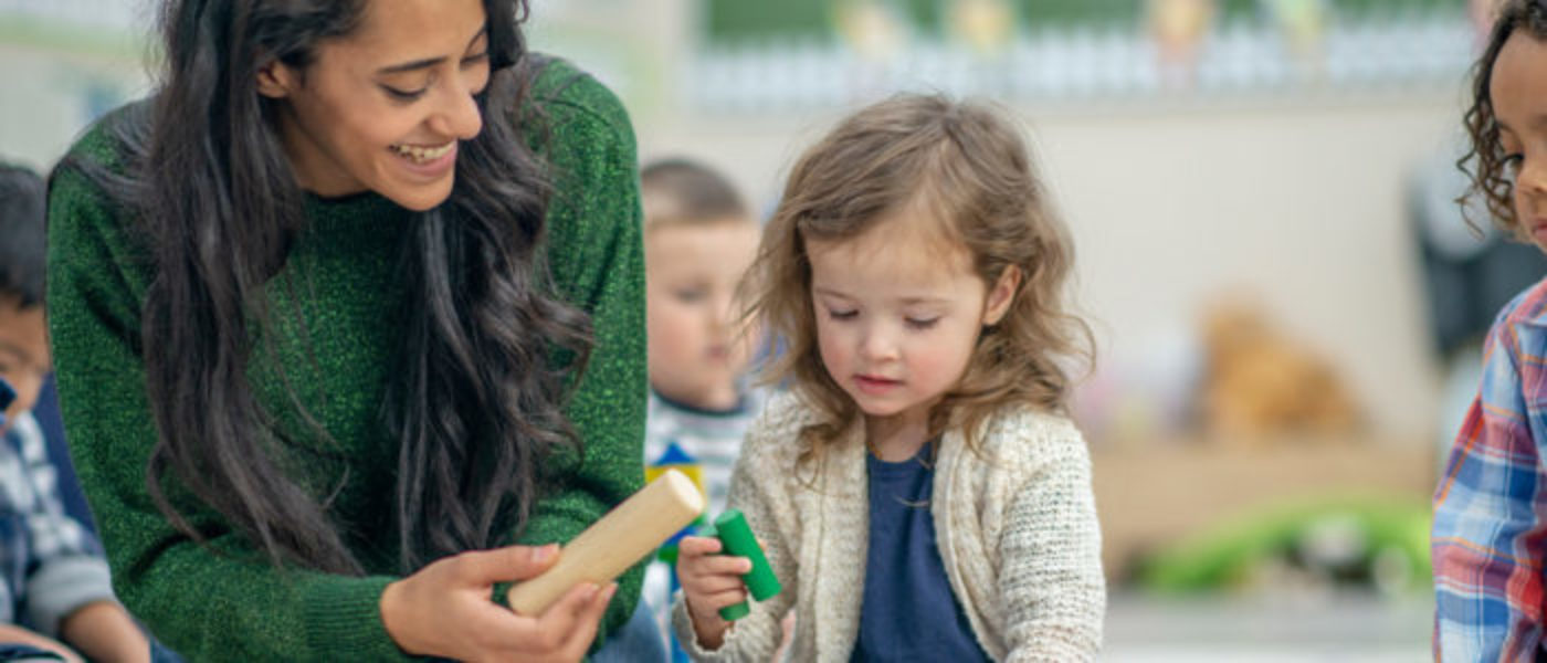 Female teacher hands a wooden block to a young child